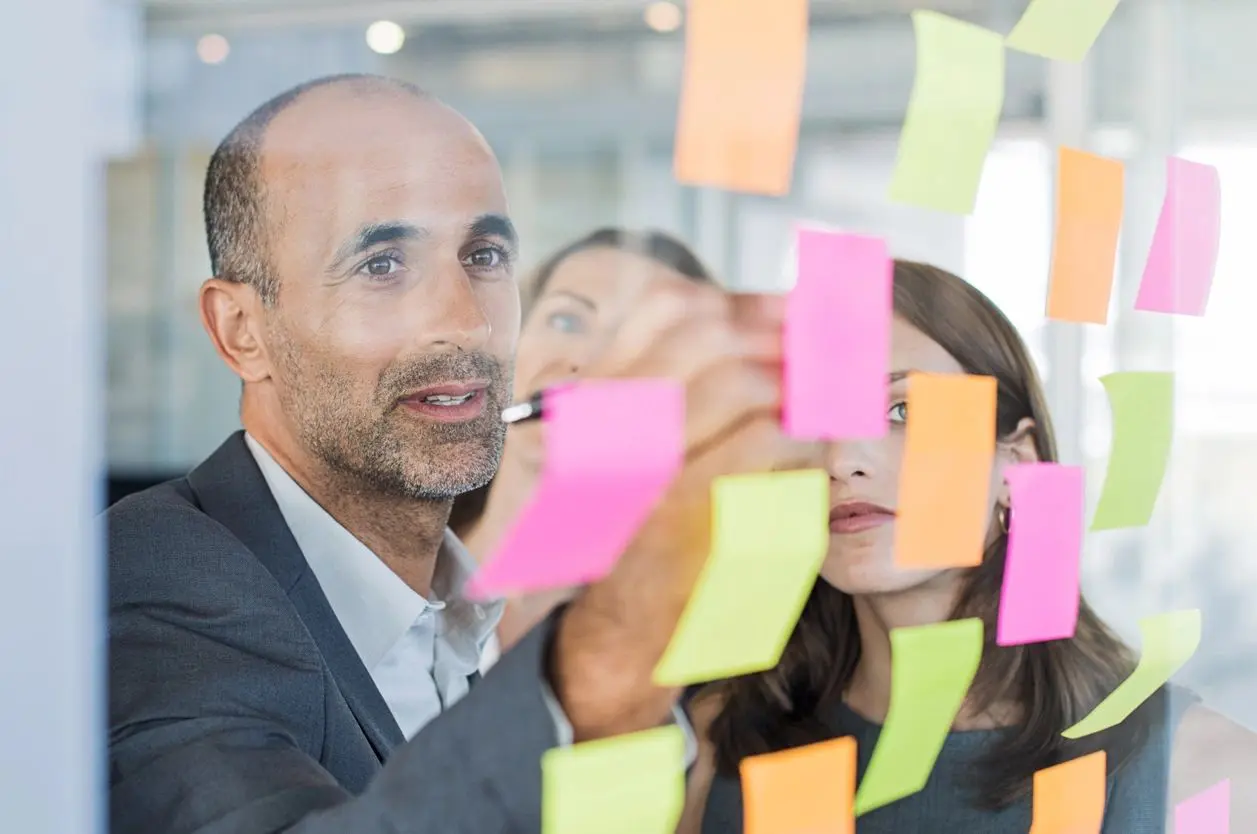 A man and woman are looking at post it notes on the wall.